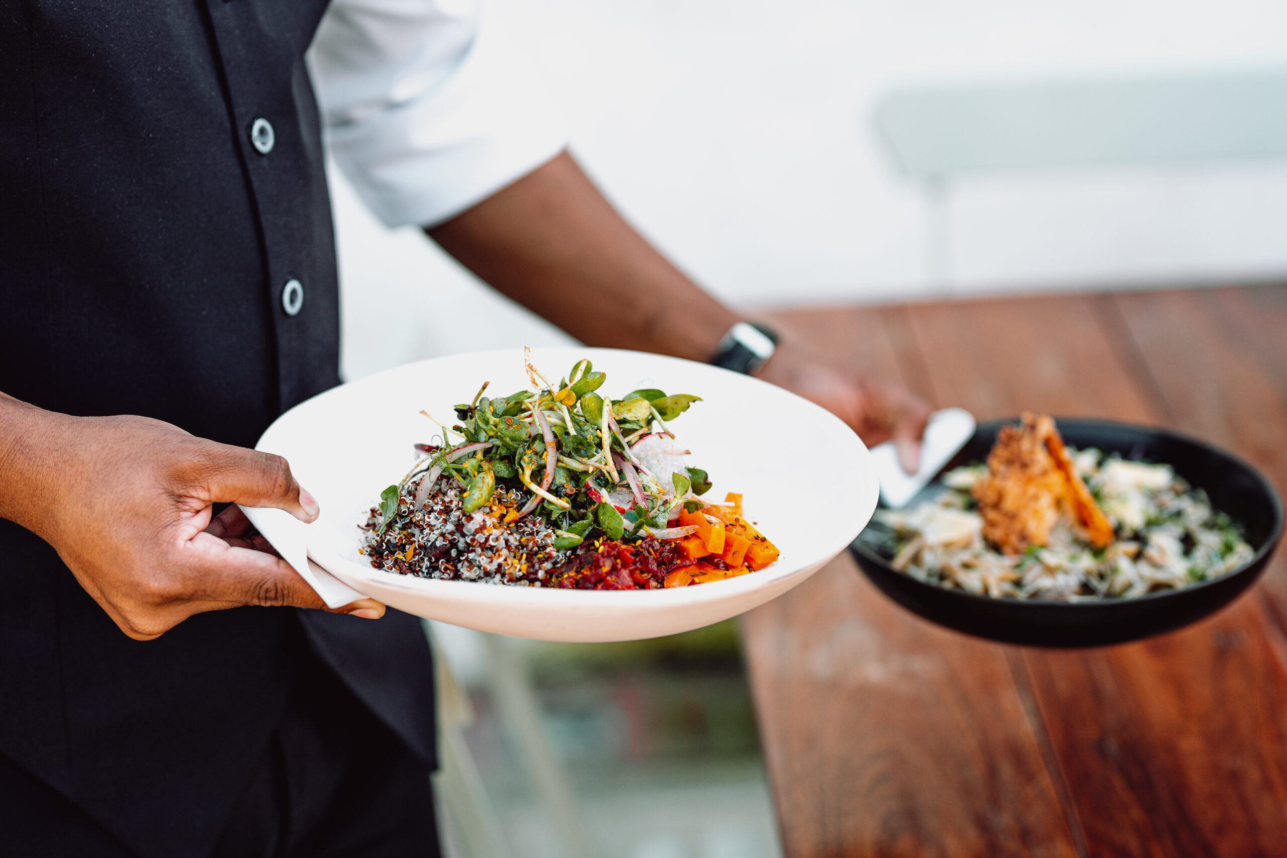 A midsection of a waiter serving two dishes on a wooden table